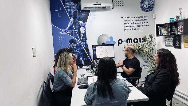 Profissionais reunidas ao redor de uma mesa no escritório da PMais.