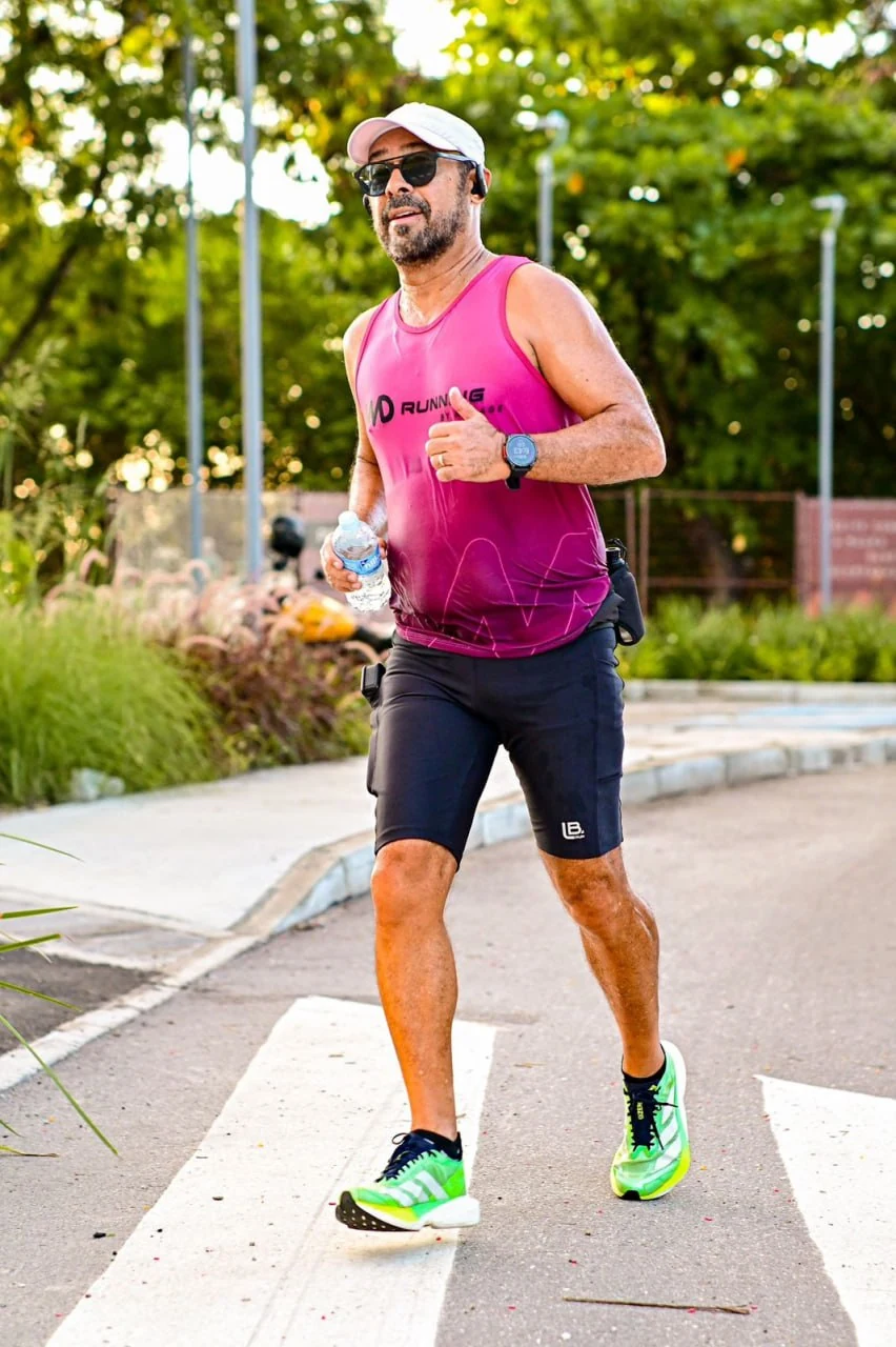 Lula Moura durante uma corrida de rua, usando viseira, óculos, camiseta rosa e tênis verdes.